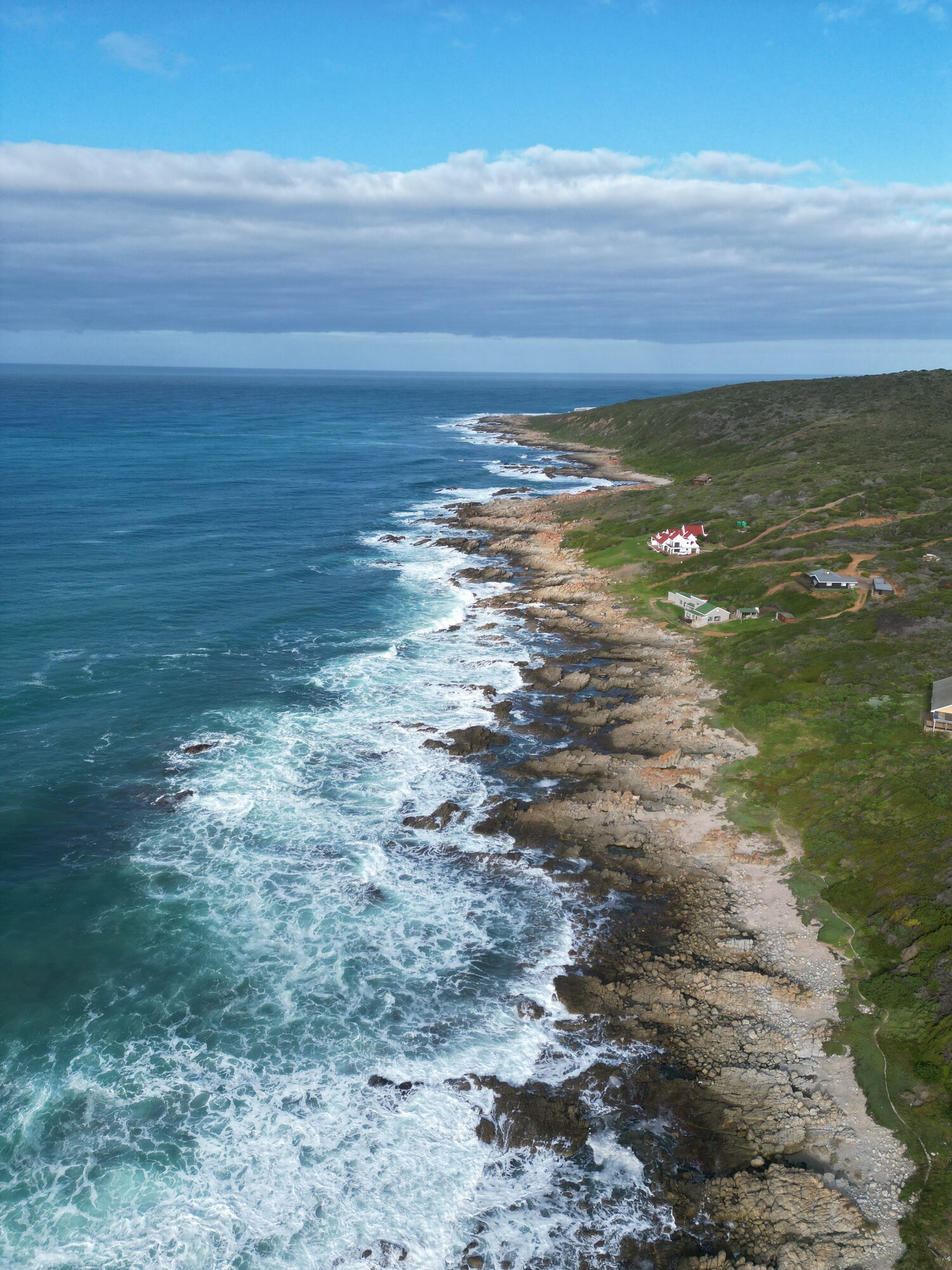 Vertical aerial of a rugged Cape coastline where whitewater meets rocky shore.