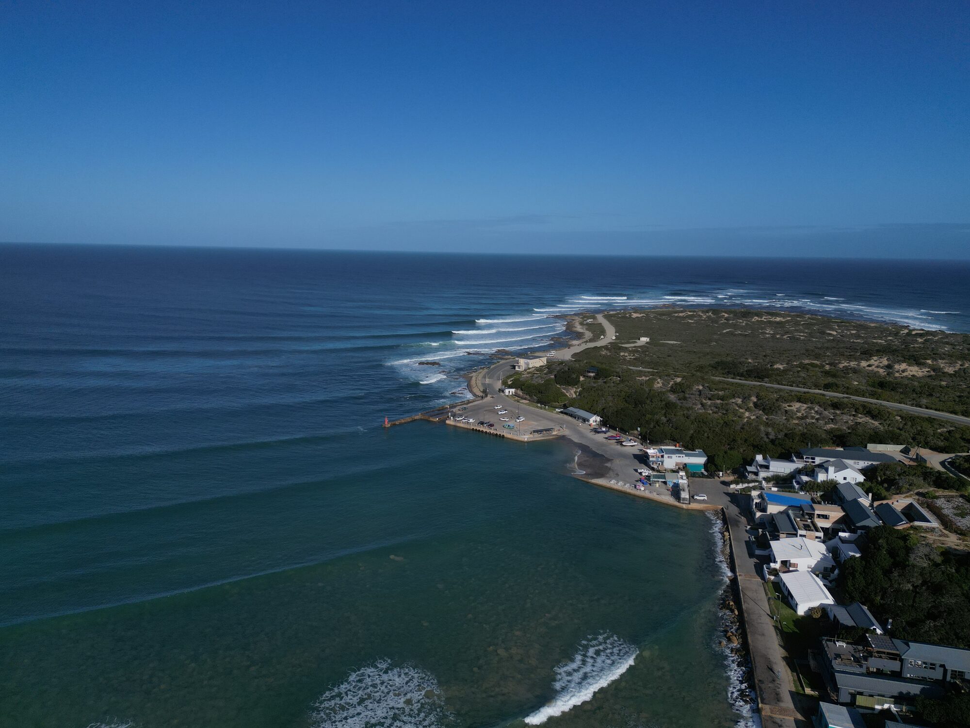 Wide aerial of a Cape estuary and point break with lines of swell wrapping in.