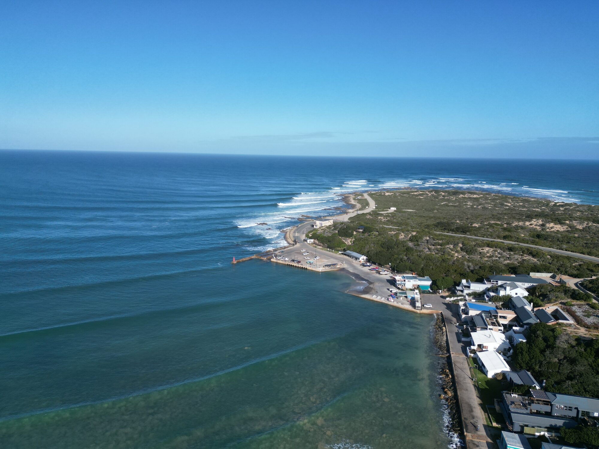 High aerial of a Cape point, harbour, and town hugging the coastline under clear sky.