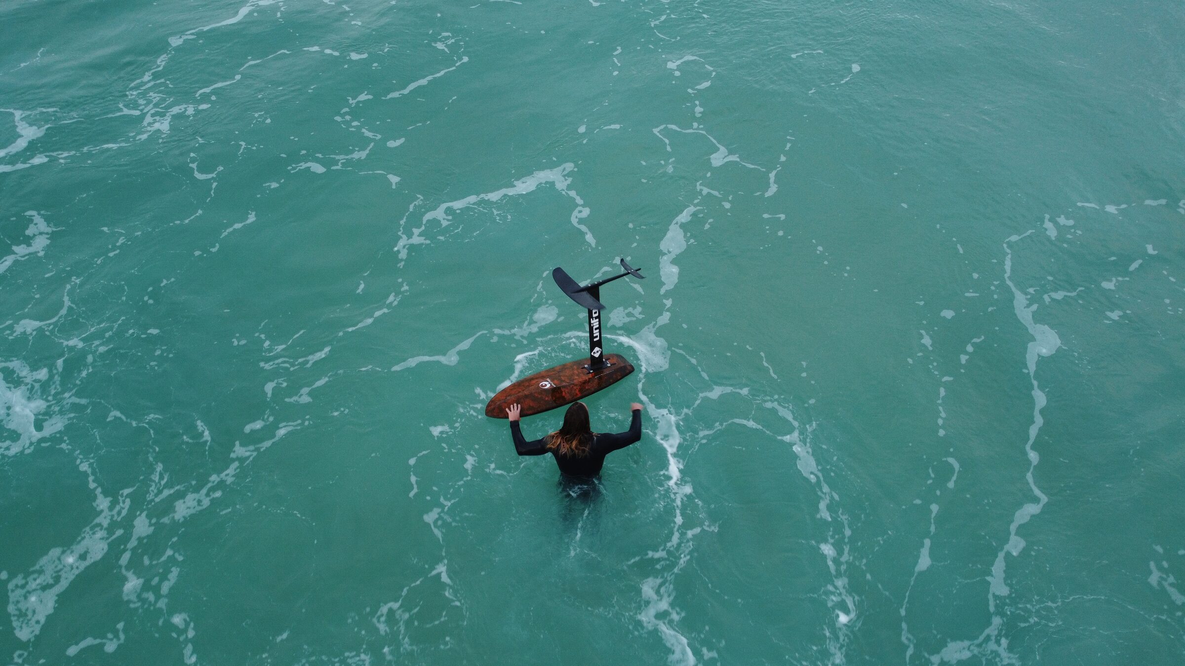 Aerial view of a lone foiler holding a board on calm turquoise water off the Cape coast.